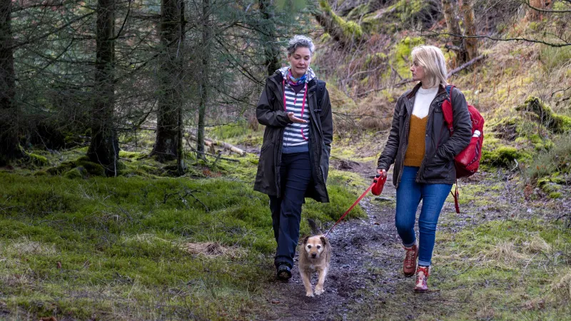 Zwei Frauen gehen zusammen mit Hund durch den Wald